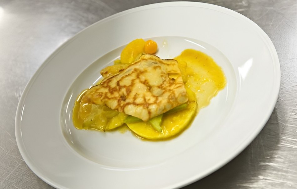A crêpe with orange sauce and fruit on a white plate, presented on a metal surface., © Hotel Neuwirtshaus A crêpe with orange sauce and fruit on a white plate, presented on a metal surface., © Hotel Neuwirtshaus