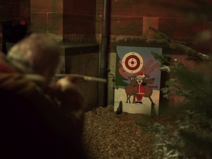 Person aims a blowpipe at a target with a reindeer motif. The scene is decorated for Christmas., © Cool-Tours StattReisen Person aims a blowpipe at a target with a reindeer motif. The scene is decorated for Christmas., © Cool-Tours StattReisen