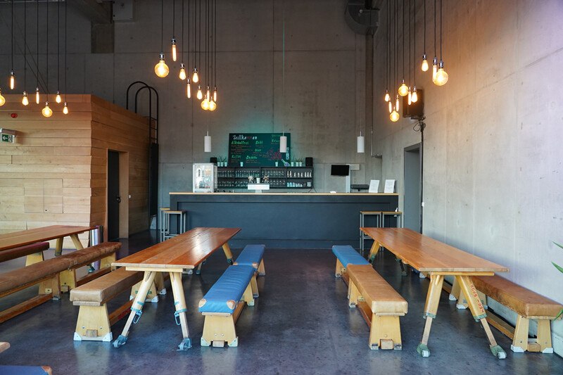 Ein modernes Caf&eacute; mit langen Holztischen, H&auml;ngelampen und einer Bar im Hintergrund. Die Einrichtung ist minimalistisch und einladend., &copy; W&uuml;rttembergische Staatstheater Stuttgart