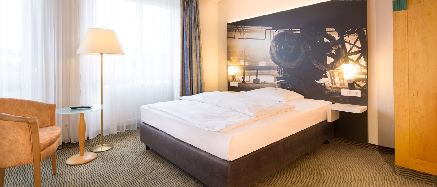 A modern single room with a large bed, an armchair, a floor lamp and a mural with an industrial motif., © Erikson Hotel