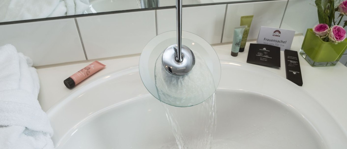 Modern bathroom with running water in the washbasin, towel, care products and flowers., © Hotel Gloria GmbH Restaurant Möhringer Hexle Modern bathroom with running water in the washbasin, towel, care products and flowers., © Hotel Gloria GmbH Restaurant Möhringer Hexle