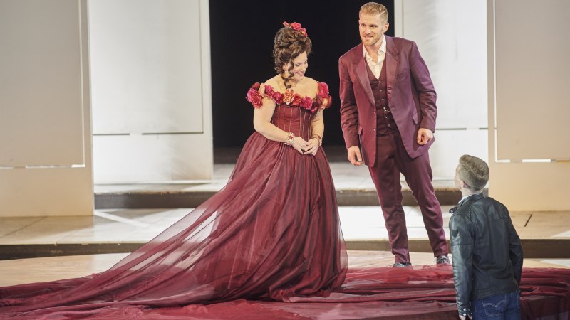Two actors in elegant clothes on the stage of an opera performance. The woman is wearing a burgundy dress, the man a matching suit., &copy; Martin Sigmund