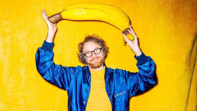 Person in blauer Jacke hält große gelbe Banane über dem Kopf vor gelbem Hintergrund., © Rosenau Kultur e.V. Person in blauer Jacke hält große gelbe Banane über dem Kopf vor gelbem Hintergrund., © Rosenau Kultur e.V.