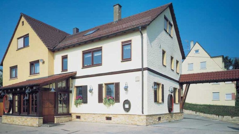 Two-storey building with a yellow and white fa&ccedil;ade and red roof tiles. A VdW banner stands in front of it. Clear blue sky in the background., &copy; Weinstube J&auml;gerhof