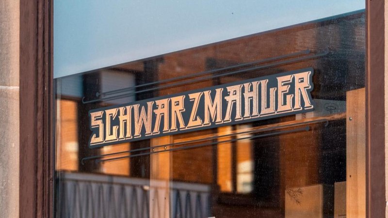 Ein Schaufenster mit dem Schriftzug 'Schwarzmahler' in stilisierter Schrift. Die Umgebung spiegelt sich im Glas., &copy; SMG, Sarah Schmid