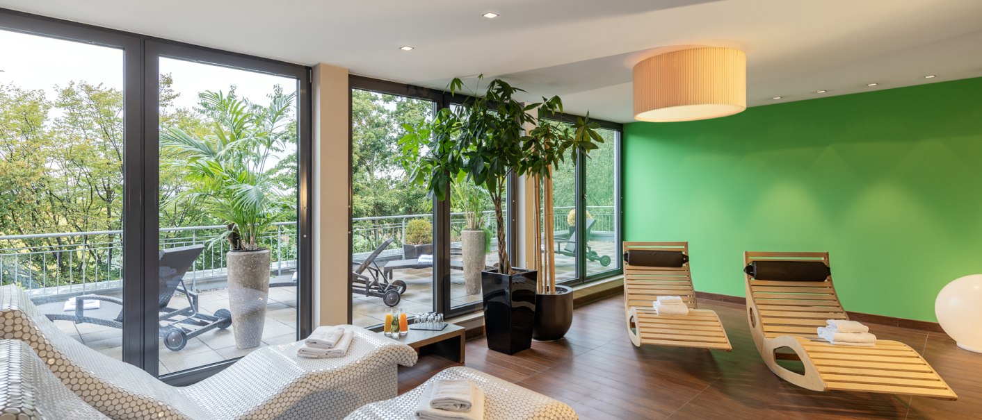Moderner Wellnessbereich mit Liegest&uuml;hlen, Pflanzen und gro&szlig;en Fenstern, die auf eine Terrasse mit weiteren Liegen blicken., &copy; NH Hotel Stuttgart Airport
