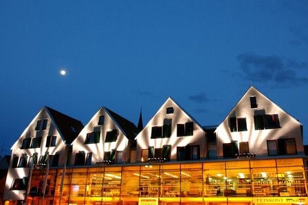 Ein modernes Gebäude mit beleuchteten Giebeln und Glasfassade bei Nacht. Der Mond ist am klaren Himmel sichtbar., © Hotel an der Stadtmauer Ein modernes Gebäude mit beleuchteten Giebeln und Glasfassade bei Nacht. Der Mond ist am klaren Himmel sichtbar., © Hotel an der Stadtmauer