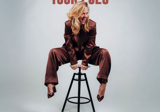 Frau in braunem Anzug sitzt l&auml;chelnd auf einem Hocker. Text k&uuml;ndigt Ricarda Hofmanns Special Interest Tour 2026 in Stuttgart an., &copy; Theaterhaus Stuttgart e.V.