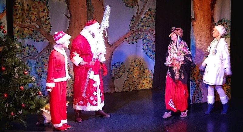 Theaterszene mit Väterchen Frost, Baba Jaga und anderen Figuren in bunten Kostümen vor einem bemalten Waldhintergrund., © Theater Atelier