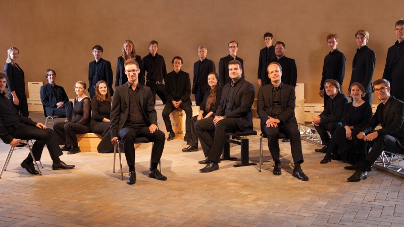 Eine Gruppe von Menschen in schwarzer Kleidung posiert in einem Raum. Einige sitzen auf Stühlen, andere stehen im Hintergrund. Der Boden ist aus Ziegelsteinen., © Seicento vocale Eine Gruppe von Menschen in schwarzer Kleidung posiert in einem Raum. Einige sitzen auf Stühlen, andere stehen im Hintergrund. Der Boden ist aus Ziegelsteinen., © Seicento vocale