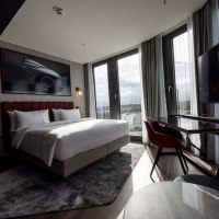 Modernes Eckzimmer mit gro&szlig;em Bett, Schreibtisch, Panoramafenstern und stilvollem Dekor. Ein Bild eines Autos h&auml;ngt an der Wand., &copy; Radisson Hotel Group