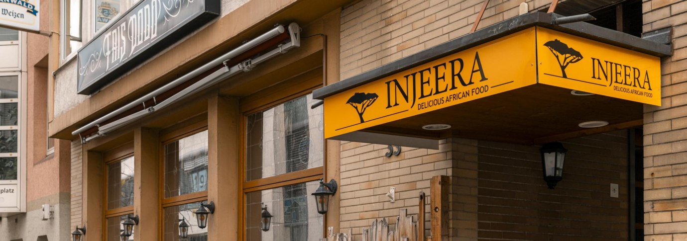 Restaurant Injeera mit gelbem Schild und Holzzaun, bietet afrikanische K&uuml;che an. Au&szlig;enansicht mit Laternen und Pflanzen., &copy; SMG, Sarah Schmid