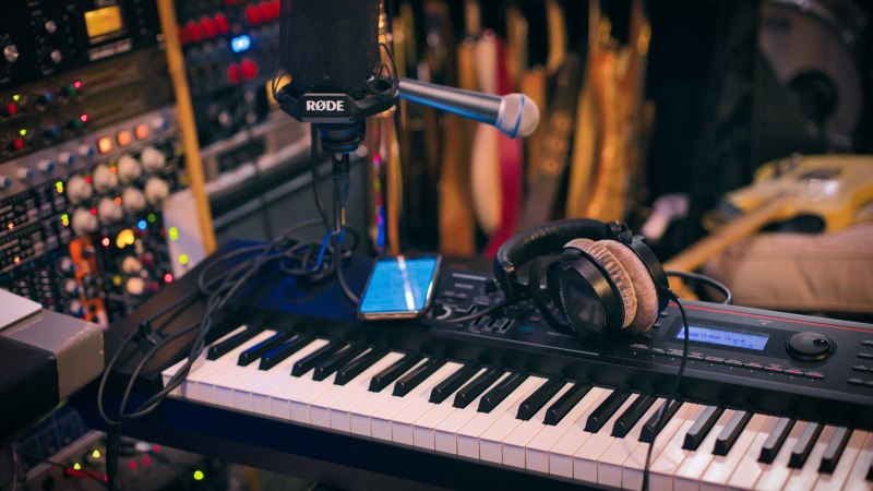 Ein Musikstudio mit einem Keyboard, Mikrofon, Kopfhörern und Mischpulten. Gitarren sind im Hintergrund sichtbar., © @caught_in_joy