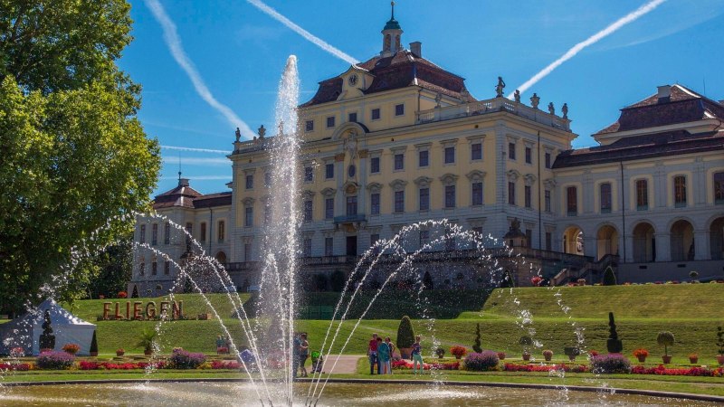 The Ludwigsburg Residential Palace with a large fountain in the foreground. The sky is blue with contrails, surrounded by manicured gardens., © Tourismus & Events Ludwigsburg