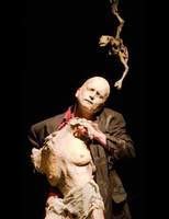 Ein Performer in einem dunklen Anzug h&auml;lt eine groteske Skulptur auf einer B&uuml;hne. Die Szene wirkt dramatisch und k&uuml;nstlerisch., &copy; FITZ Das Theater animierter Formen