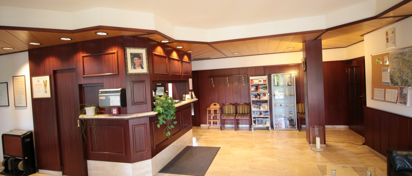 A reception hall with wooden walls, a reception desk, plants and a seating area. Pictures and certificates hang on the wall., © TOMAS A reception hall with wooden walls, a reception desk, plants and a seating area. Pictures and certificates hang on the wall., © TOMAS