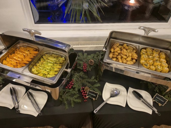 Ein Buffet mit verschiedenen Speisen in W&auml;rmebeh&auml;ltern, dekoriert mit Tannenzweigen und roten Beeren. Teller und Besteck sind bereitgestellt., &copy; Cool-Tours StattReisen