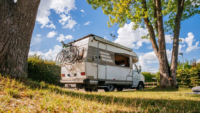 Ein Wohnmobil mit Fahrrädern am Heck steht auf einem grünen Stellplatz unter Bäumen. Der Himmel ist blau mit weißen Wolken., © Stuttgart-Marketing GmbH, Thomas Niedermüller