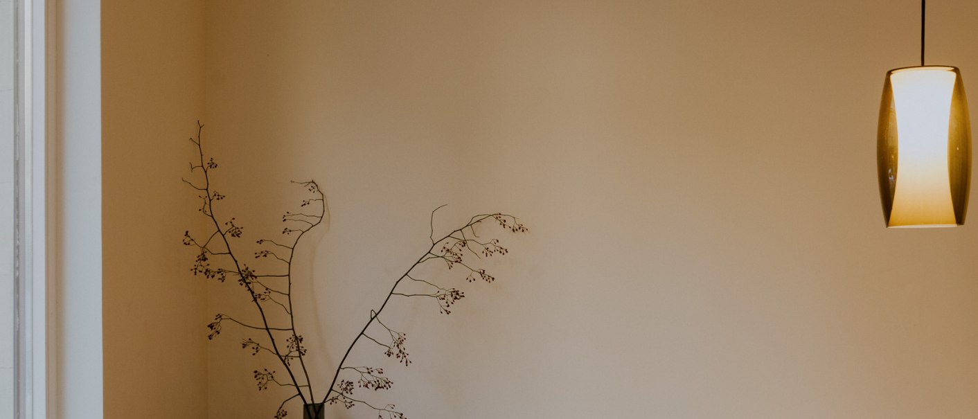 Minimalistisch eingerichteter Raum mit einem hellen Sofa, einer Holzbank mit B&uuml;chern, einer Vase mit Zweigen und einer modernen H&auml;ngelampe., &copy; Peter Oliver Wolff / DAS EDITH