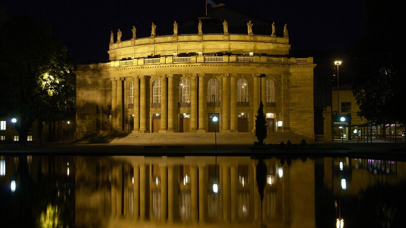 Beleuchtetes historisches Geb&auml;ude mit S&auml;ulen, nachts aufgenommen. Die Fassade spiegelt sich im Wasser davor wider., &copy; W&uuml;rttembergische Staatstheater Stuttgart