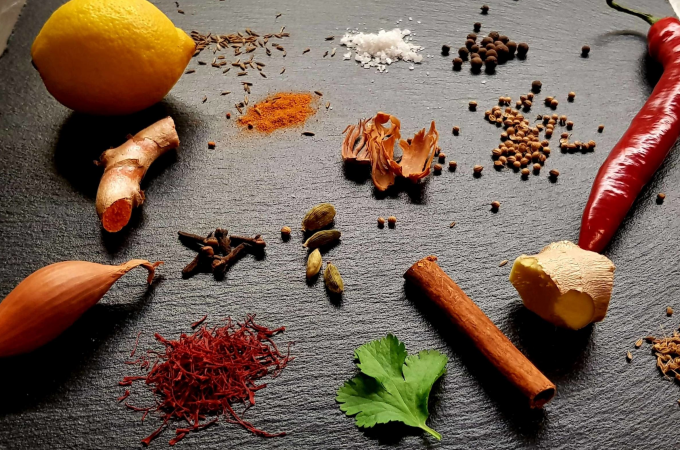 Lemon, ginger, chili, shallot, cinnamon stick, cardamom, cloves, saffron, parsley and various spices arranged on a dark surface., &copy; Kultweine-Kochwelten-Kunst&uuml;cke - Kochschule Sonja Lenz