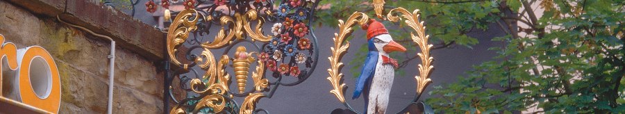 An artistically decorated sign with a penguin and figures, surrounded by floral ornaments, hangs on a wall on Eugensplatz., &copy; Stuttgart-Marketing GmbH