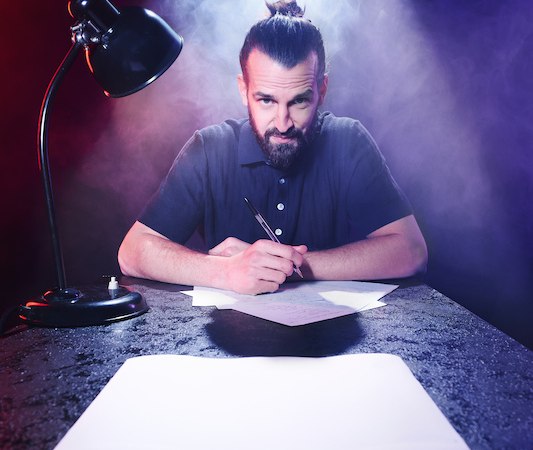 Ein Mann mit Bart und Dutt sitzt an einem Tisch, schreibt auf Papier. Buntes Licht und Rauch umgeben ihn, eine Lampe leuchtet von der Seite., © Rosenau Kultur e.V. Ein Mann mit Bart und Dutt sitzt an einem Tisch, schreibt auf Papier. Buntes Licht und Rauch umgeben ihn, eine Lampe leuchtet von der Seite., © Rosenau Kultur e.V.