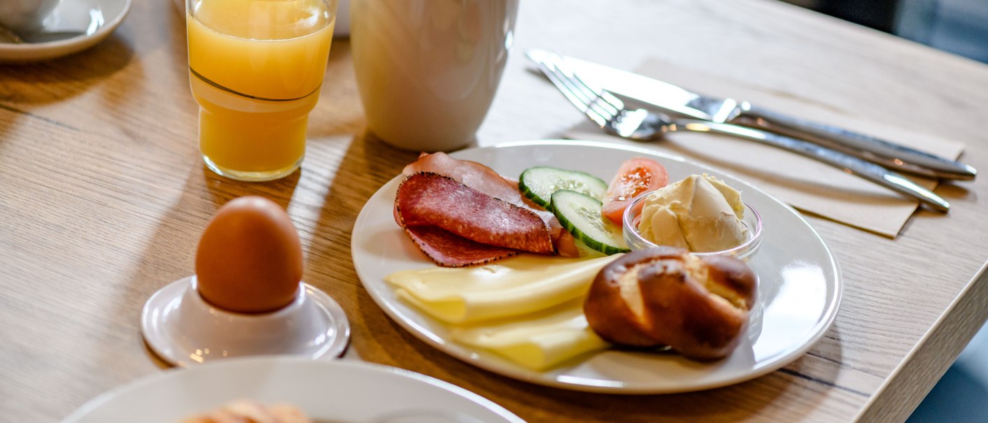Frühstück im Hilton Garden Inn: Teller mit Wurst, Käse, Gemüse, Brötchen und Butter. Dazu ein Glas Orangensaft, Kaffee und ein gekochtes Ei., © Hilton Garden Inn Stuttgart Neckarpark