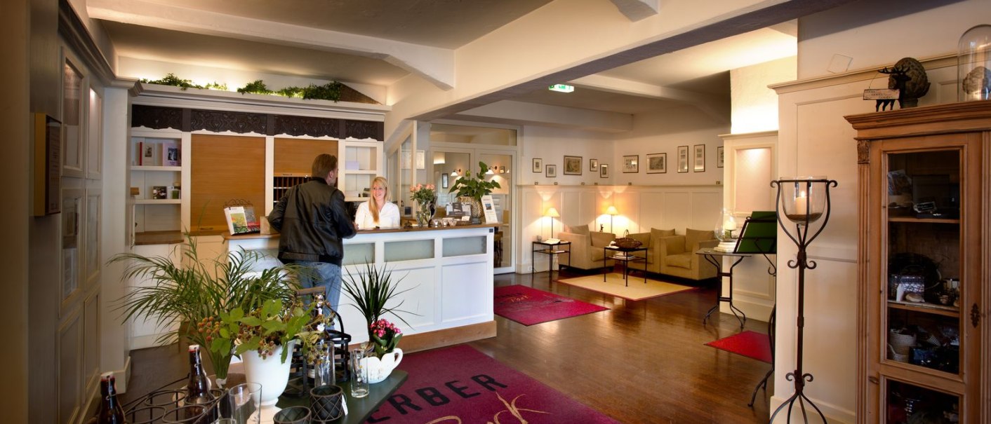 Hotel reception with a guest and a member of staff. The lobby is comfortably furnished with sofas, plants and decorations., © TOMAS