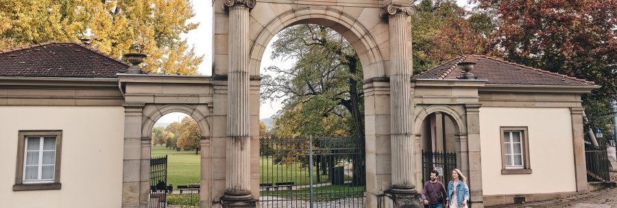 Entrance gate to Rosenstein Park with the inscription 'Rosenstein'. Two people walk past, surrounded by autumnal trees., &copy; SMG, Christoph D&uuml;pper