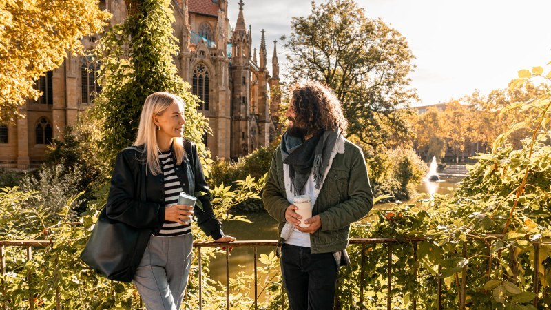 Zwei Personen unterhalten sich vor der Johanneskirche am Feuersee, umgeben von herbstlichem Laub und Sonnenschein., © SMG, Sarah Schmid Zwei Personen unterhalten sich vor der Johanneskirche am Feuersee, umgeben von herbstlichem Laub und Sonnenschein., © SMG, Sarah Schmid