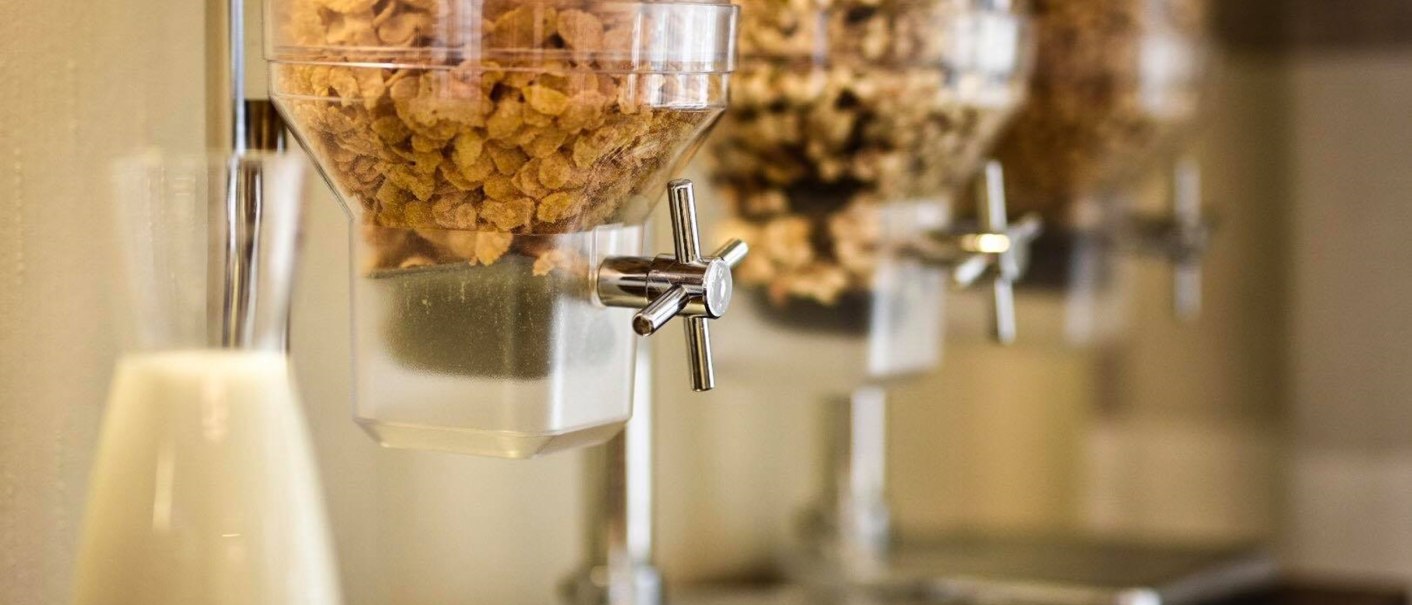 Cereal dispenser with different varieties and a milk carafe on a breakfast table., &copy; TOMAS