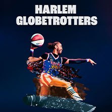 Ein Spieler der Harlem Globetrotters wirft einen Basketball vor blauem Hintergrund. Dynamische Pose und bunte Uniform., © links im Bild