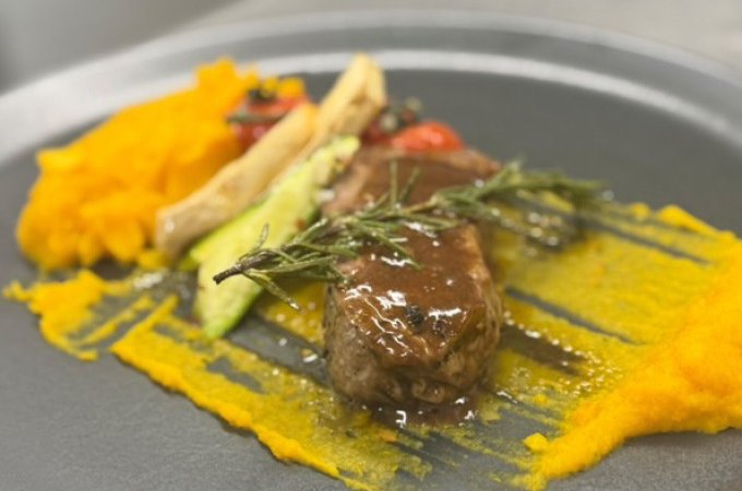 Ein kunstvoll angerichtetes Gericht mit Fleisch, K&uuml;rbisp&uuml;ree und Gem&uuml;se auf einem grauen Teller, dekoriert mit Rosmarin., &copy; Cool-Tours StattReisen