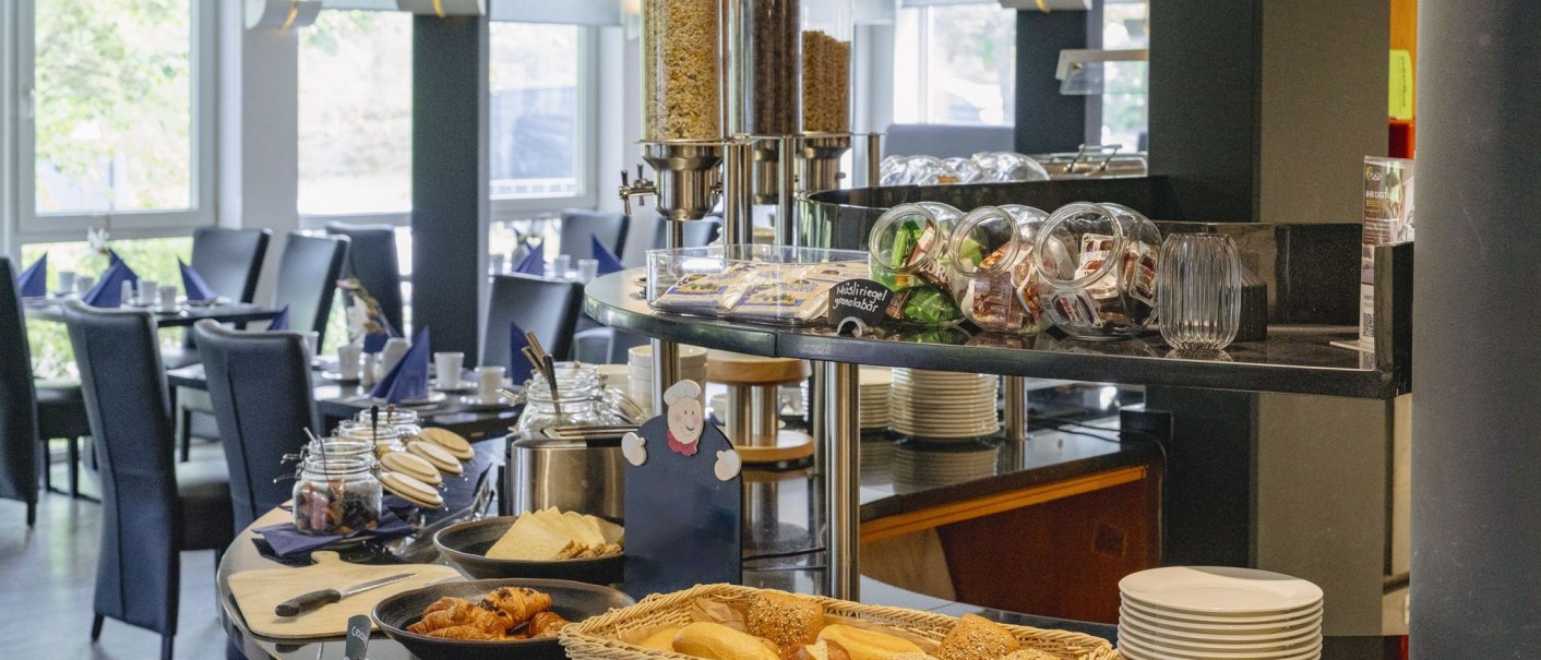A breakfast buffet with bread rolls, croissants, muesli and jam in a bright dining room with laid tables., © Plaza INN Stuttgart-Filderstadt A breakfast buffet with bread rolls, croissants, muesli and jam in a bright dining room with laid tables., © Plaza INN Stuttgart-Filderstadt