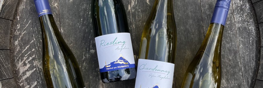 Vier Weinflaschen liegen auf einem Holzfass. Die Etiketten zeigen "Riesling" und "Chardonnay" vom Weinhof am Württemberg., © Weinhof Zaiß