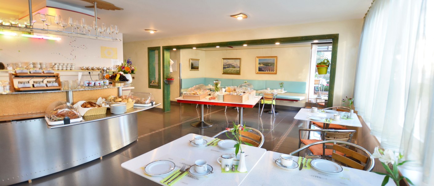 Ein heller Frühstücksraum mit gedeckten Tischen, einem Buffet mit Gebäck und einer gemütlichen Atmosphäre., © Abalon Hotel Ideal Ein heller Frühstücksraum mit gedeckten Tischen, einem Buffet mit Gebäck und einer gemütlichen Atmosphäre., © Abalon Hotel Ideal