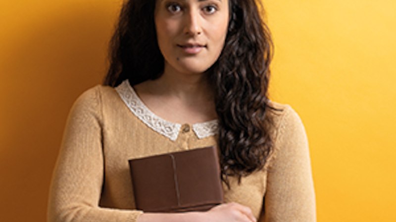 Eine Frau mit lockigem Haar hält ein braunes Tagebuch vor einem gelben Hintergrund. Sie trägt einen beigefarbenen Pullover mit Spitzenkragen., © Altes Schauspielhaus und Komödie im Marquardt e.V. Eine Frau mit lockigem Haar hält ein braunes Tagebuch vor einem gelben Hintergrund. Sie trägt einen beigefarbenen Pullover mit Spitzenkragen., © Altes Schauspielhaus und Komödie im Marquardt e.V.