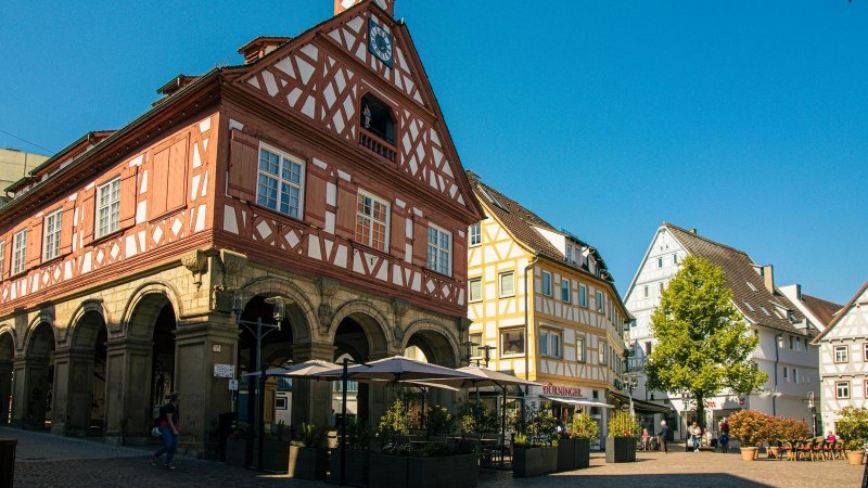 Historic half-timbered building on the market square in Waiblingen, surrounded by other half-timbered houses and an outdoor café in sunny weather., © Stuttgart-Marketing GmbH, Sarah Schmid Historic half-timbered building on the market square in Waiblingen, surrounded by other half-timbered houses and an outdoor café in sunny weather., © Stuttgart-Marketing GmbH, Sarah Schmid