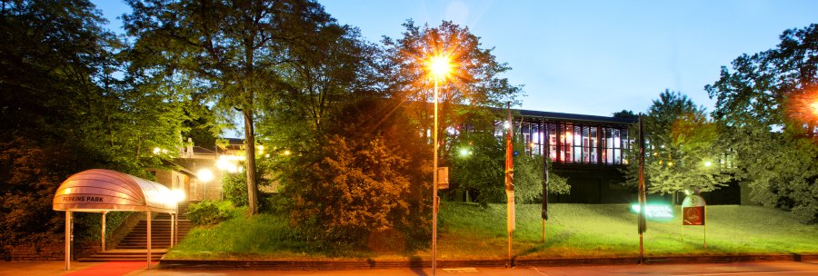 Entrance to Perkins Park at night, illuminated with a red carpet. Trees and a modern building can be seen in the background., &copy; PerkinsPark
