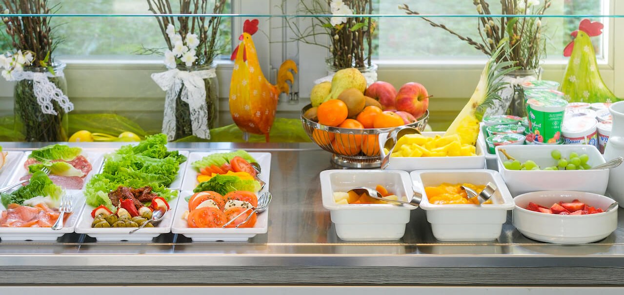 Ein Frühstücksbuffet mit frischem Obst, Gemüse, Joghurt und dekorativen Hühnerfiguren. Im Hintergrund sind Blumenarrangements zu sehen., © Hetzel Hotel Stuttgart Ein Frühstücksbuffet mit frischem Obst, Gemüse, Joghurt und dekorativen Hühnerfiguren. Im Hintergrund sind Blumenarrangements zu sehen., © Hetzel Hotel Stuttgart