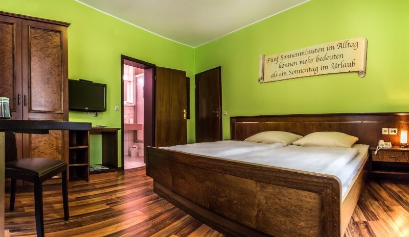 Double room with green-painted walls, wooden bed, desk, TV and a saying on the wall. Bathroom in the background., &copy; TOMAS