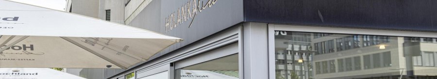 Exterior view of the Holanka Bar with large parasols. People sitting and standing in the outdoor area. Modern buildings in the background., &copy; SMG, Sarah Schmid