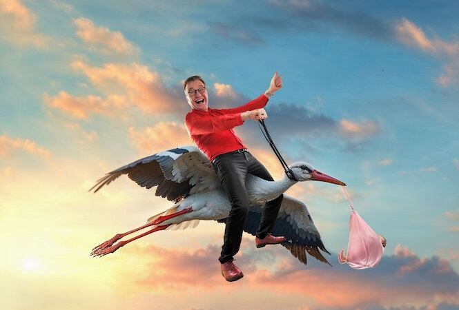 A man in a red shirt rides happily on a stork carrying a bundle in front of a colorful sky with clouds., © Renitenztheater Stuttgart e.V. A man in a red shirt rides happily on a stork carrying a bundle in front of a colorful sky with clouds., © Renitenztheater Stuttgart e.V.