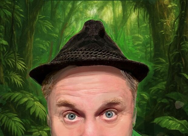A man in a green suit and hat pulls a funny face in front of a jungle-like background., &copy; Renitenztheater Stuttgart e.V.