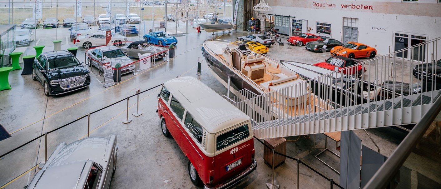 Ausstellungshalle mit verschiedenen Autos, Booten und Motorrädern. Im Vordergrund ein roter VW-Bus, im Hintergrund diverse Fahrzeuge und Boote., © V8 HOTEL