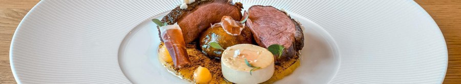 Gourmetgericht mit Entenbrust, dekorativ angerichtet auf einem weißen Teller. Beilagen und Soßen kunstvoll platziert, auf einem Holztisch serviert., © New Josch, Stuttgart Gourmetgericht mit Entenbrust, dekorativ angerichtet auf einem weißen Teller. Beilagen und Soßen kunstvoll platziert, auf einem Holztisch serviert., © New Josch, Stuttgart
