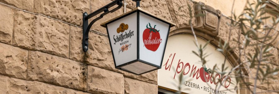 Ein Schild mit Sch&ouml;fferhofer-Logo und Tomatenmotiv h&auml;ngt an einer Steinwand vor dem Restaurant 'il pomodoro'., &copy; SMG, Sarah Schmid