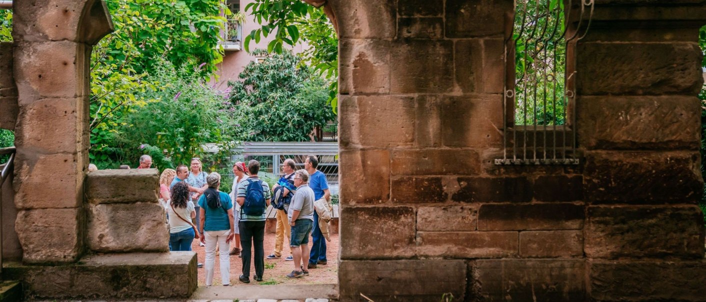 Eine Gruppe von Menschen steht in einem begrünten Innenhof, umgeben von alten Steinmauern. Im Hintergrund sind Pflanzen und ein Gebäude zu sehen., © Thomas Niedermüller Eine Gruppe von Menschen steht in einem begrünten Innenhof, umgeben von alten Steinmauern. Im Hintergrund sind Pflanzen und ein Gebäude zu sehen., © Thomas Niedermüller