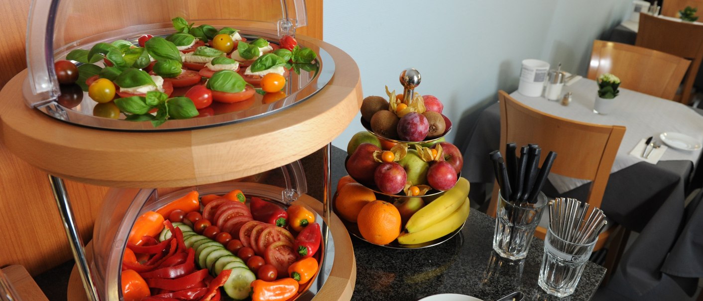 A buffet with a vegetable platter and a fruit basket. Tomatoes, peppers and cucumbers are on the platter, while bananas and oranges are in the basket., © TOMAS